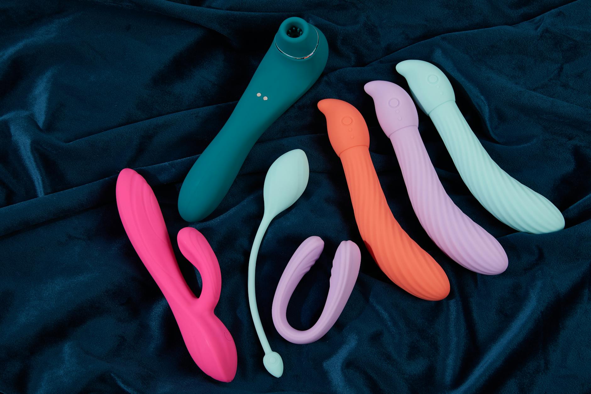 Array of colorful silicone clitoral vibrators and suction toys displayed on dark fabric