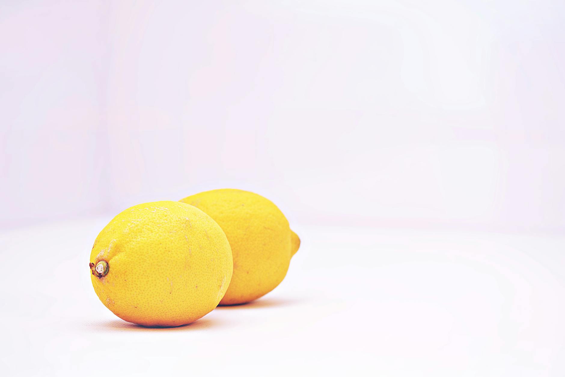 Hand holding a fresh lemon on soft pink background, symbolizing renewed sensation and gentle recovery