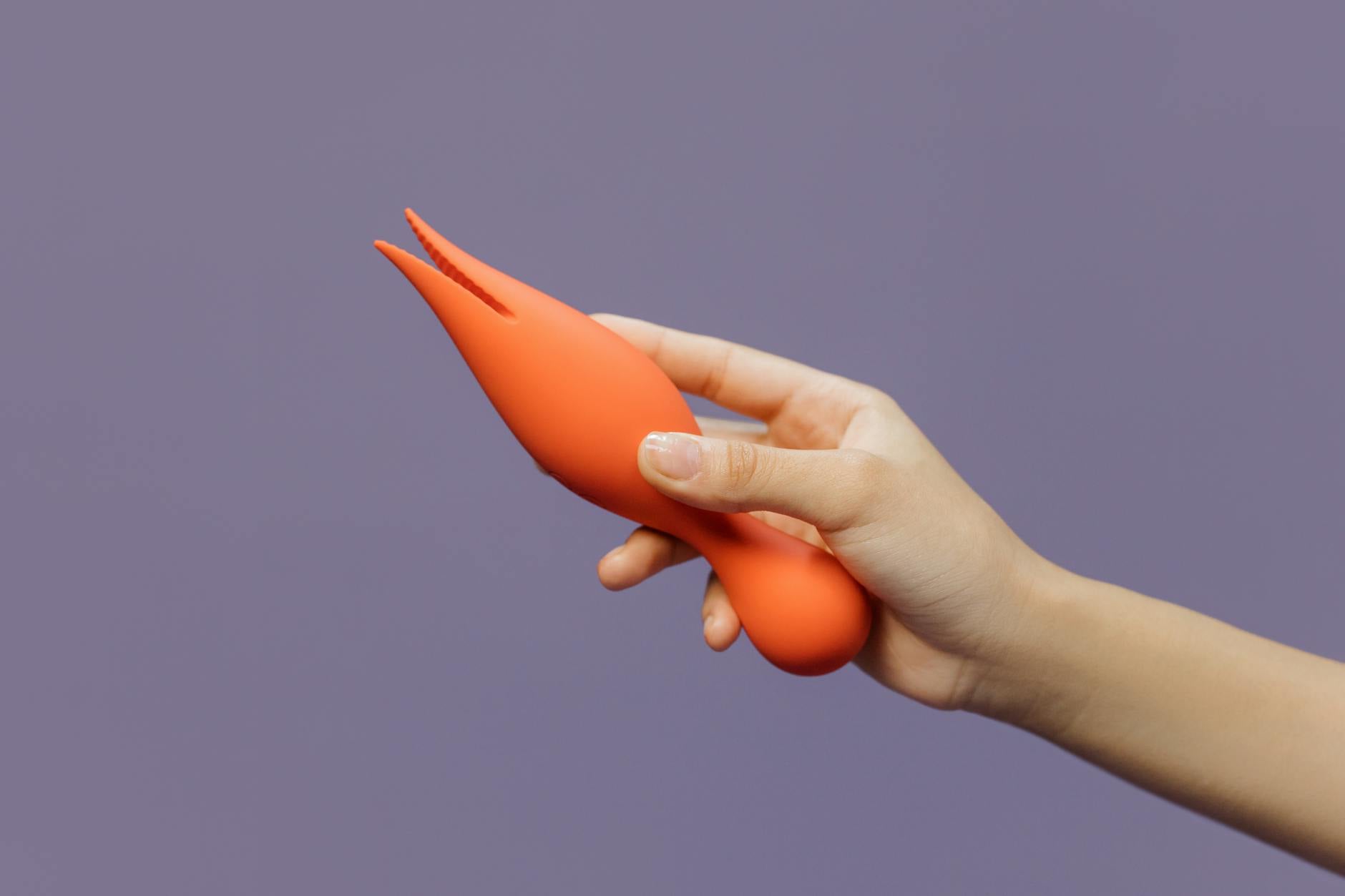 Hand holding a bright lemon-colored vibrator against a minimalist purple background, symbolizing modern intimacy