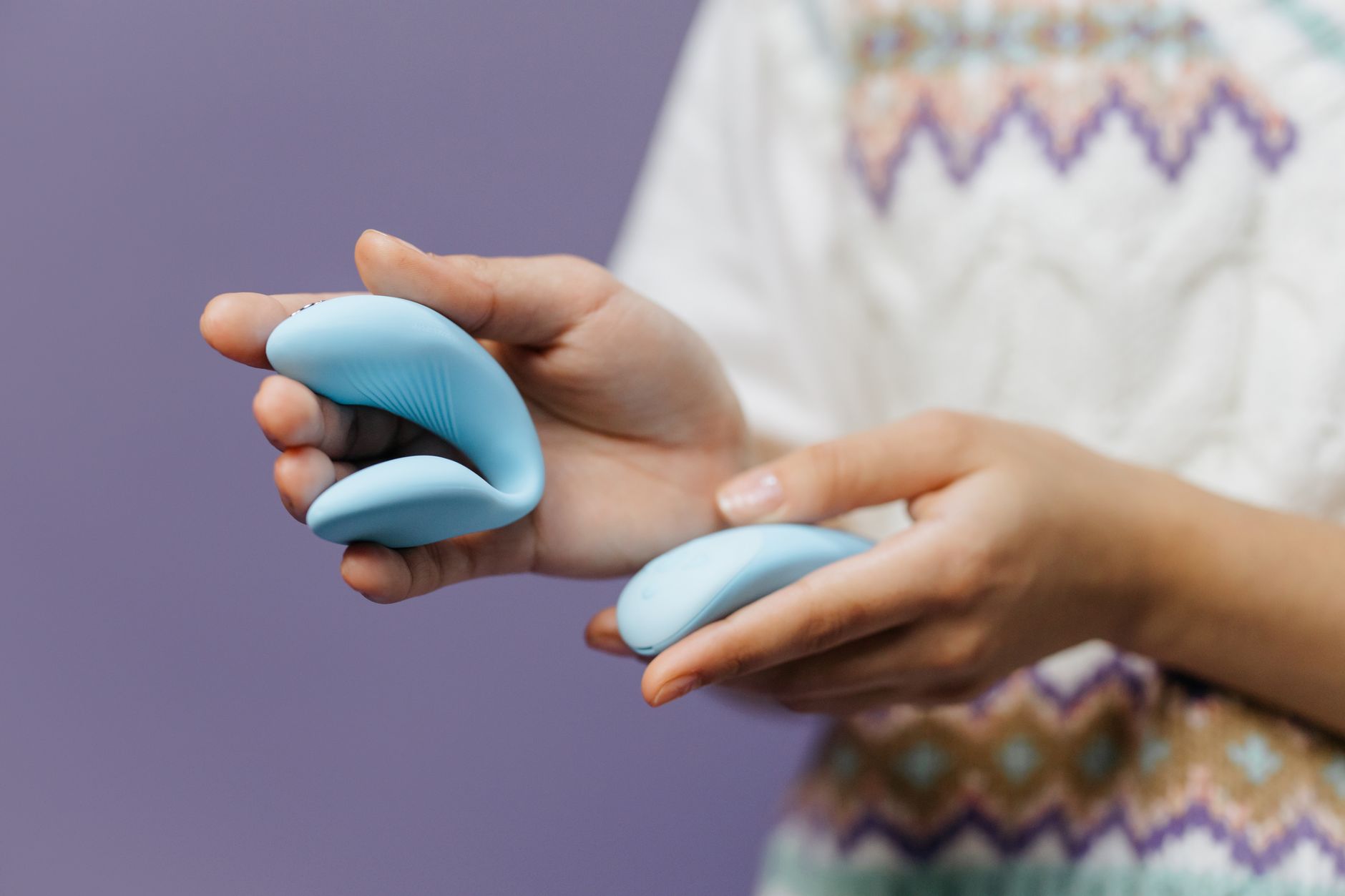 Mains tenant une vibratrice bleue contre un fond violet