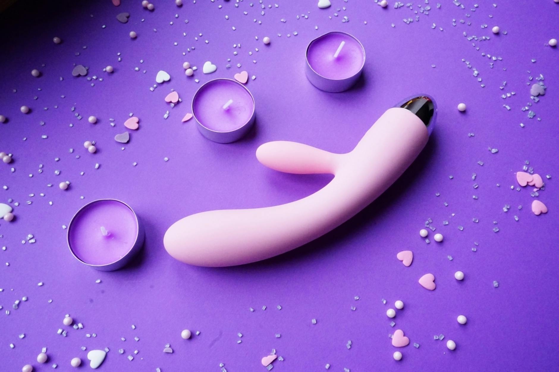 Pink vibrator on romantic surface with candles, symbolizing comfortable solo exploration and personal pleasure